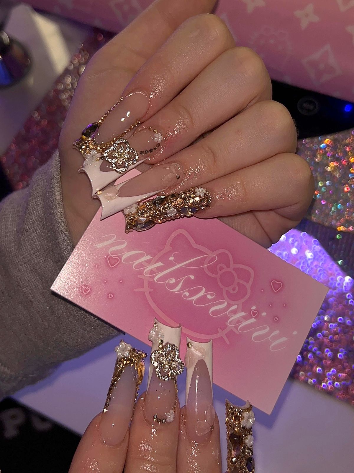 A nails x viivi business card held by a hand wearing a gold rhinestone set